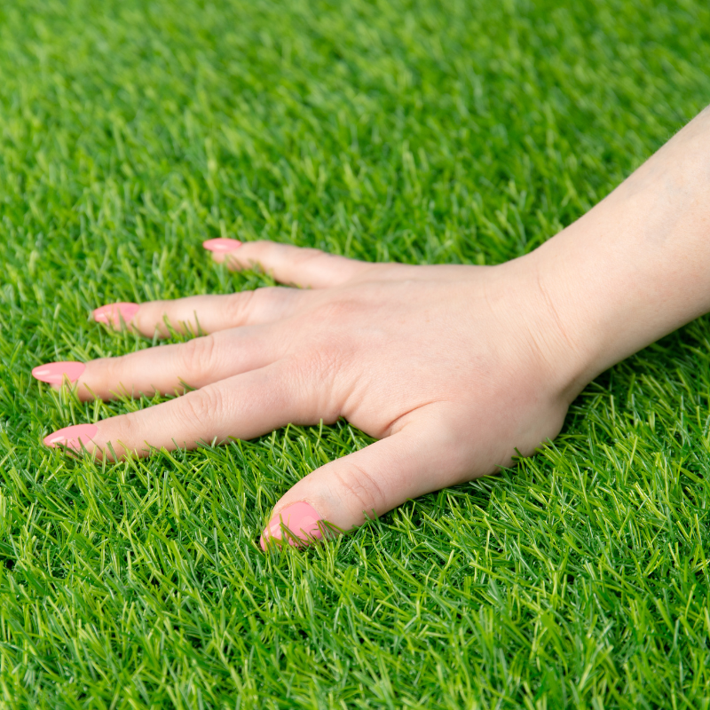 kobieca dłoń dotyka sztucznej zielonej trawy